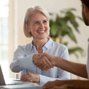 Smiling mature saleswoman handshake businessman client customer at business meeting